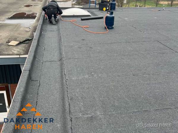 Dakdekker repareert bitumen dakbedekking op groot plat dak in Haren